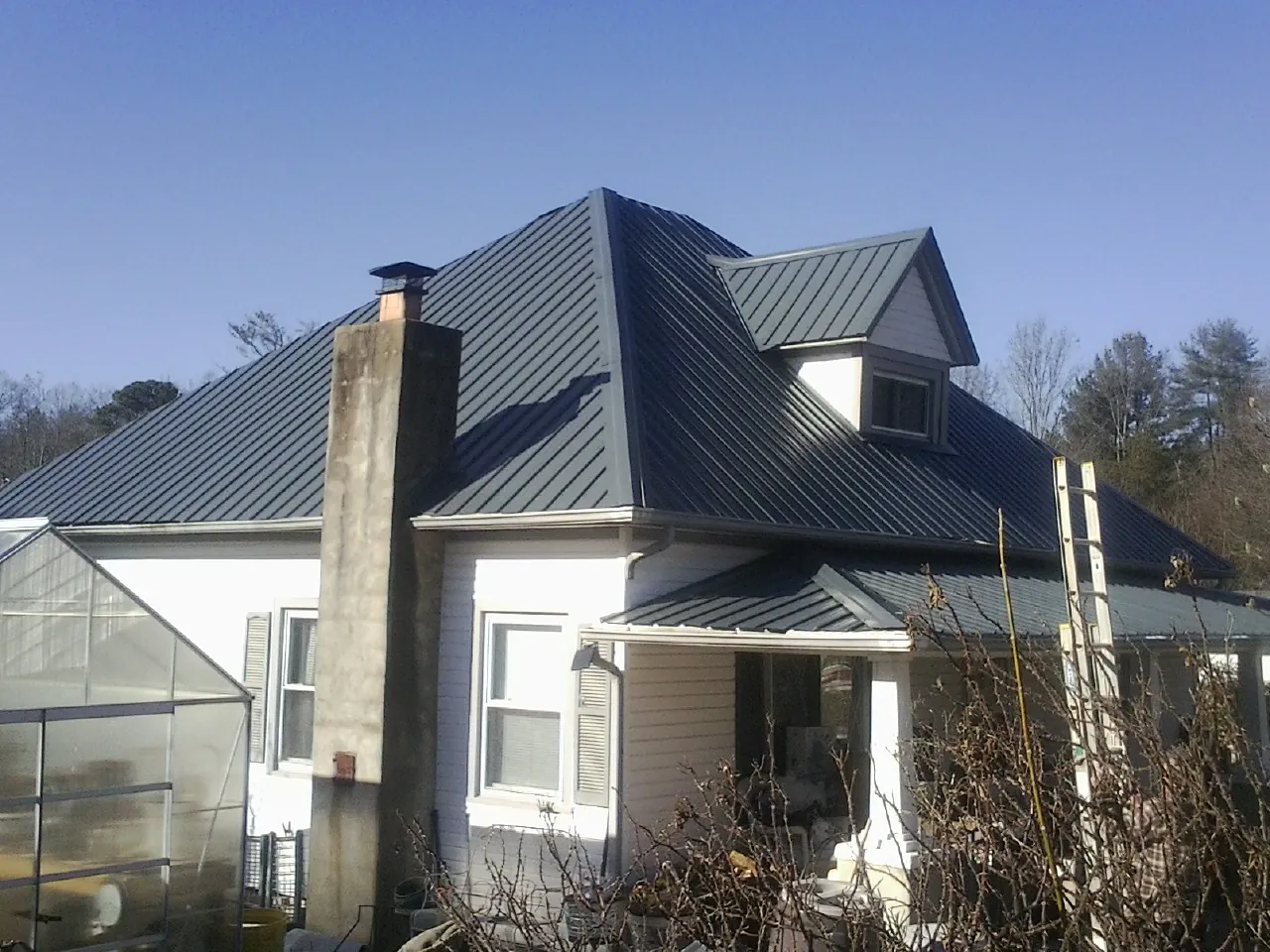 Dark blue standing seam metal roof on a white farmhouse with dormer — Slate & Tile Roof Repair by Roofing Brothers in Center Point