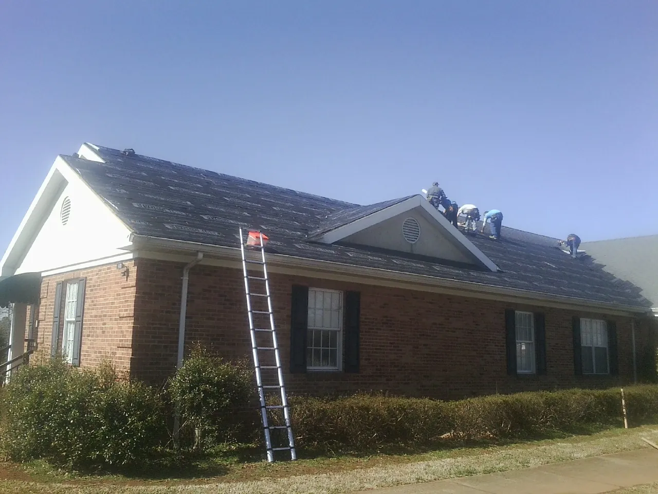 Crew tearing shingles off a brick ranch roof with a ladder set — Emergency Roof Repair work by our crew in Center Point