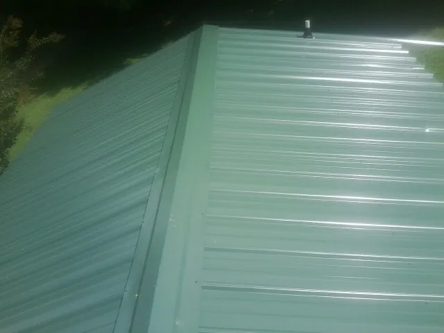 New green metal panels meeting at the ridge of a roof — Flat Roof Repair work by our crew in Center Point