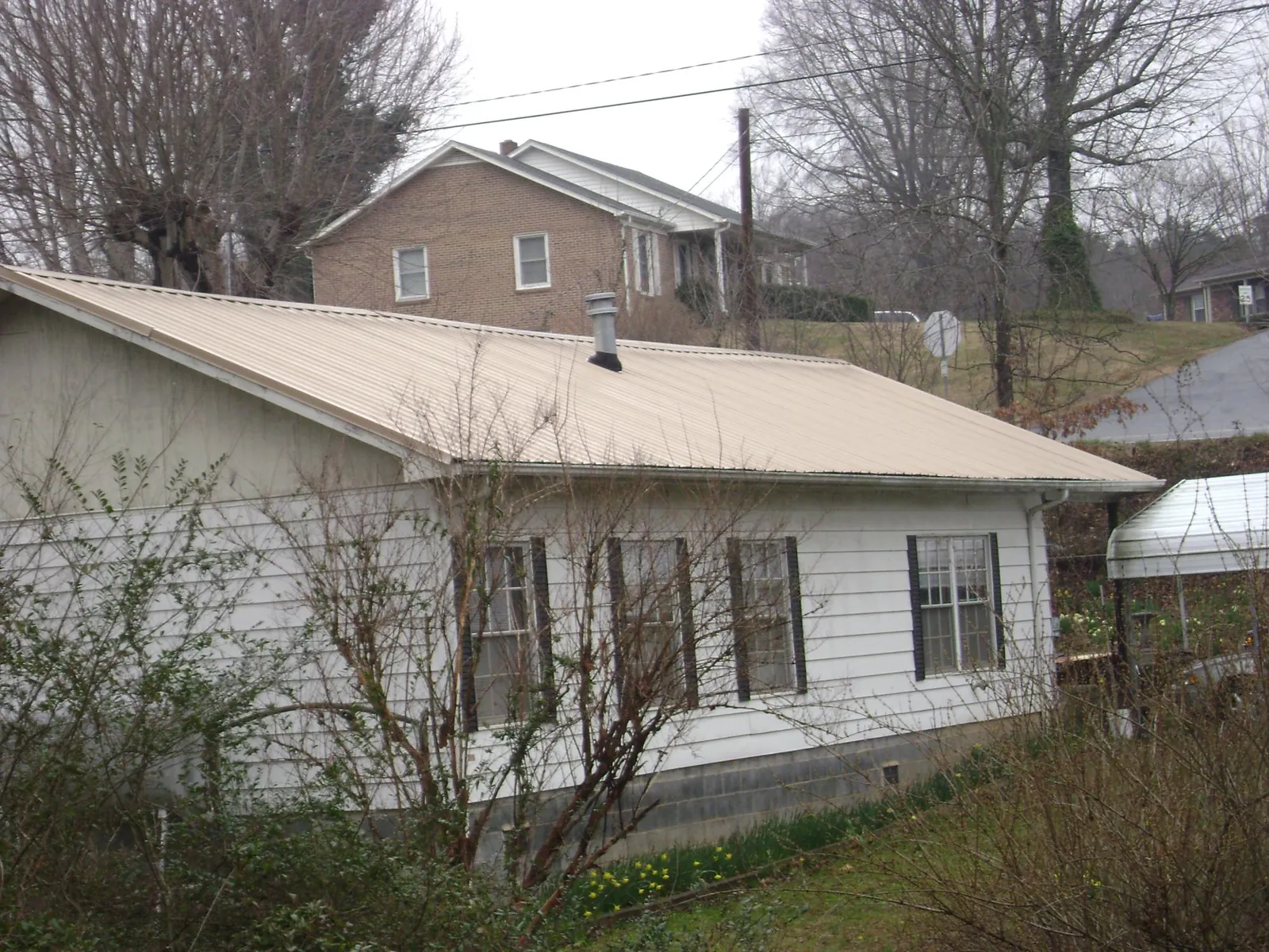 Tan metal roof on a white sided house set into a hillside — Commercial Roofing by Roofing Brothers in Center Point